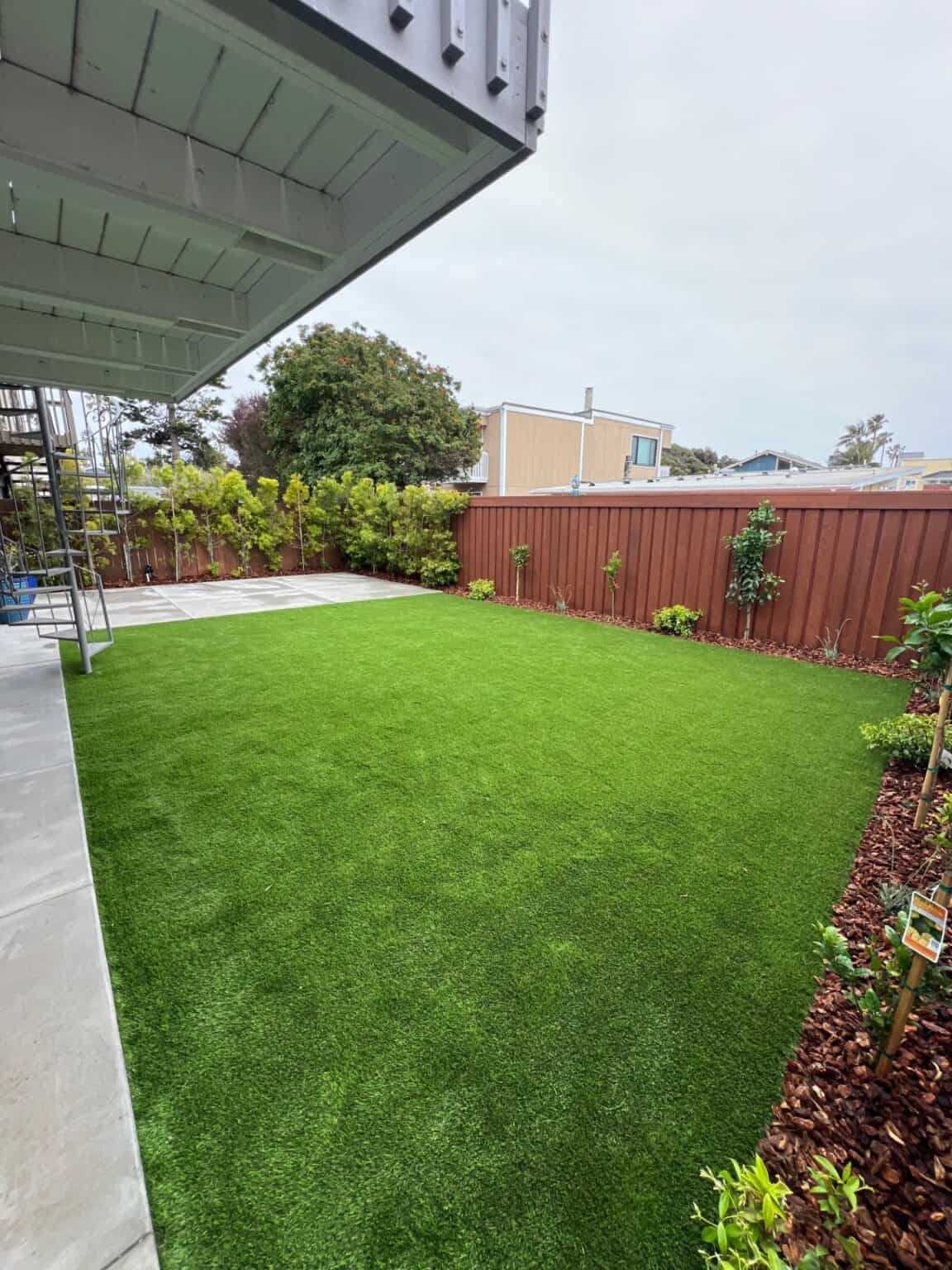 Finished backyard with artificial turf laid flat and level beside a paved edge