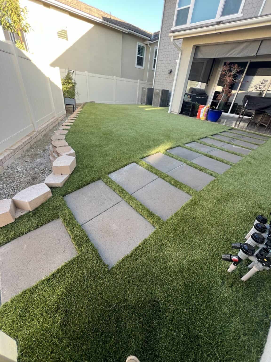 Finished backyard with artificial turf bordered by pavers