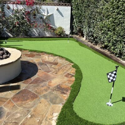 Finished backyard putting green with a flag, fringe turf, and planting beds